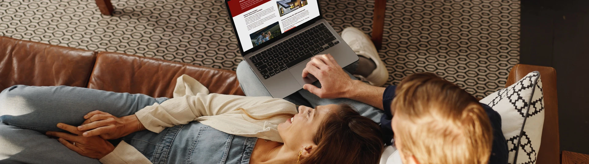 Junges Pärchen liegt auf der Couch und informiert sich am Laptop über die BSH Finanzierung.