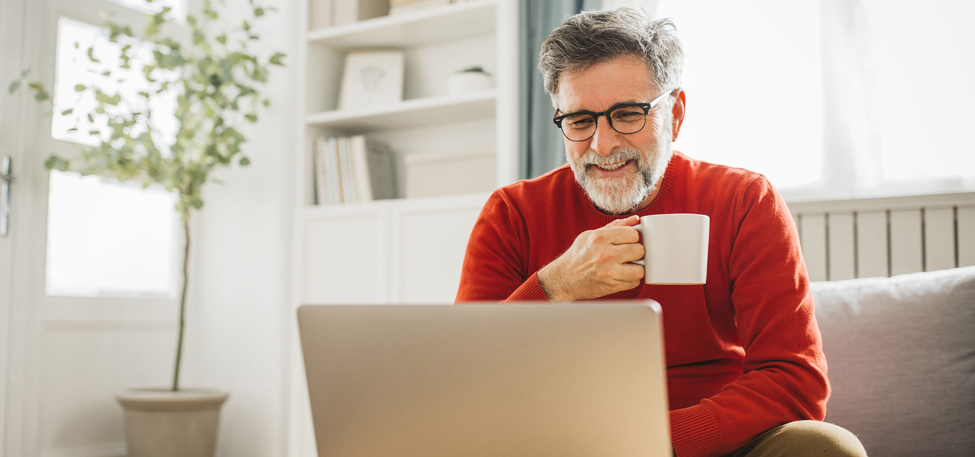 Geschäftsmann prüft am Laptop Finanzierungsoptionen und genießt eine Kaffeepause