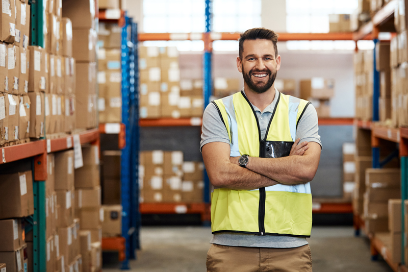 Mitarbeiter in Logistikhalle mit Regalen und Kartons – hoher Energiebedarf für Beleuchtung und Betrieb