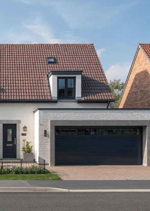Modernes Einfamilienhaus mit rotem Ziegeldach, weiß gestrichener Fassade, dunklen Fensterrahmen und Garage. Vor dem Haus befindet sich ein gepflegter Vorgarten mit Sträuchern, Blumen und kleinem Baum