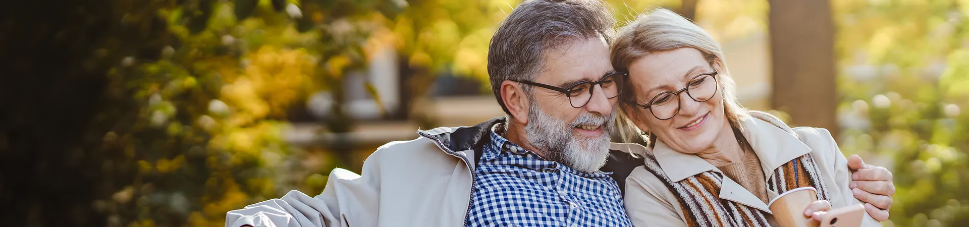 Reifes Pärchen sitzt auf einer Bank in der Natur und informiert sich über die Finanzierung ihrer Photovoltaikanlage.
