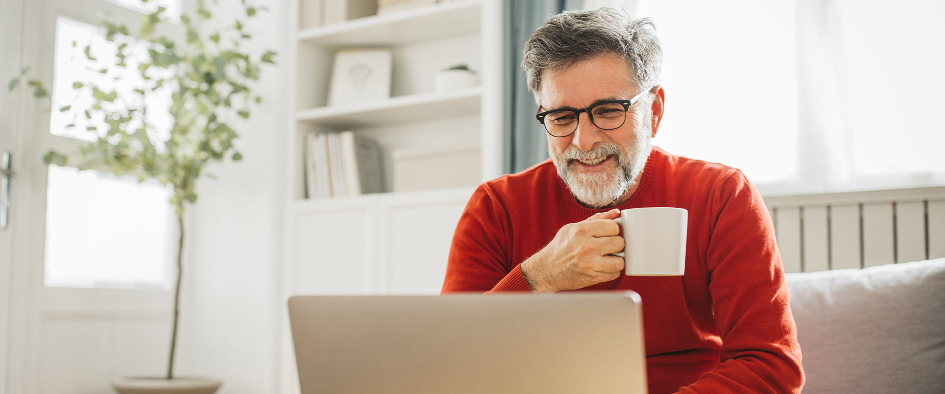 Geschäftsmann prüft am Laptop Finanzierungsoptionen und genießt eine Kaffeepause
