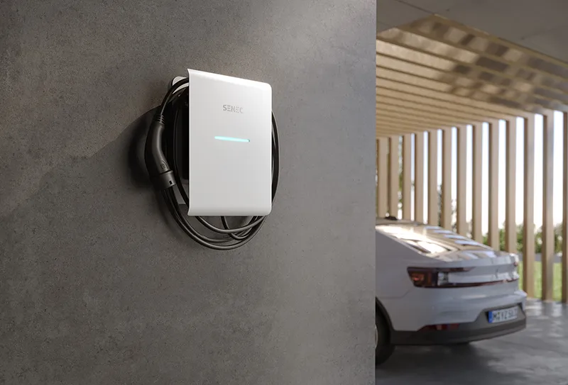 Das Bild zeigt eine SENEC Wallbox an einer Hauswand im Carport-Bereich. Im Hintergrund ist ein Elektroauto zu sehen. Das Motiv eignet sich für Inhalte rund um Wallbox-Förderung, private Ladeinfrastruktur und E-Mobilität im eigenen Zuhause.