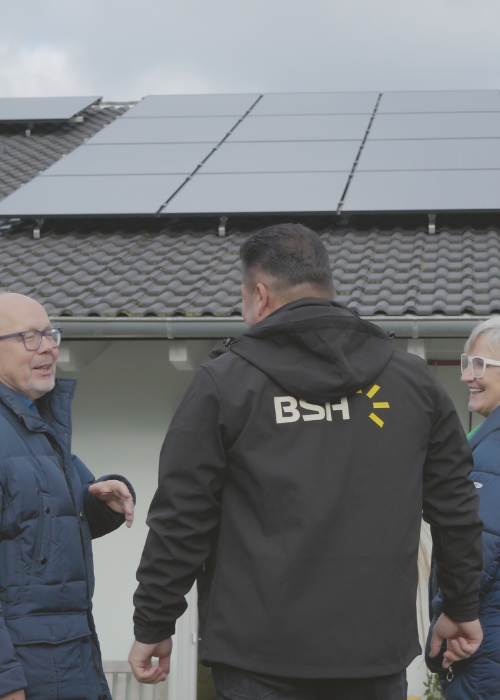 Glückliches älteres Ehepaar mit Fachberater vor ihrem Einfamilienhaus mit PV-Anlage