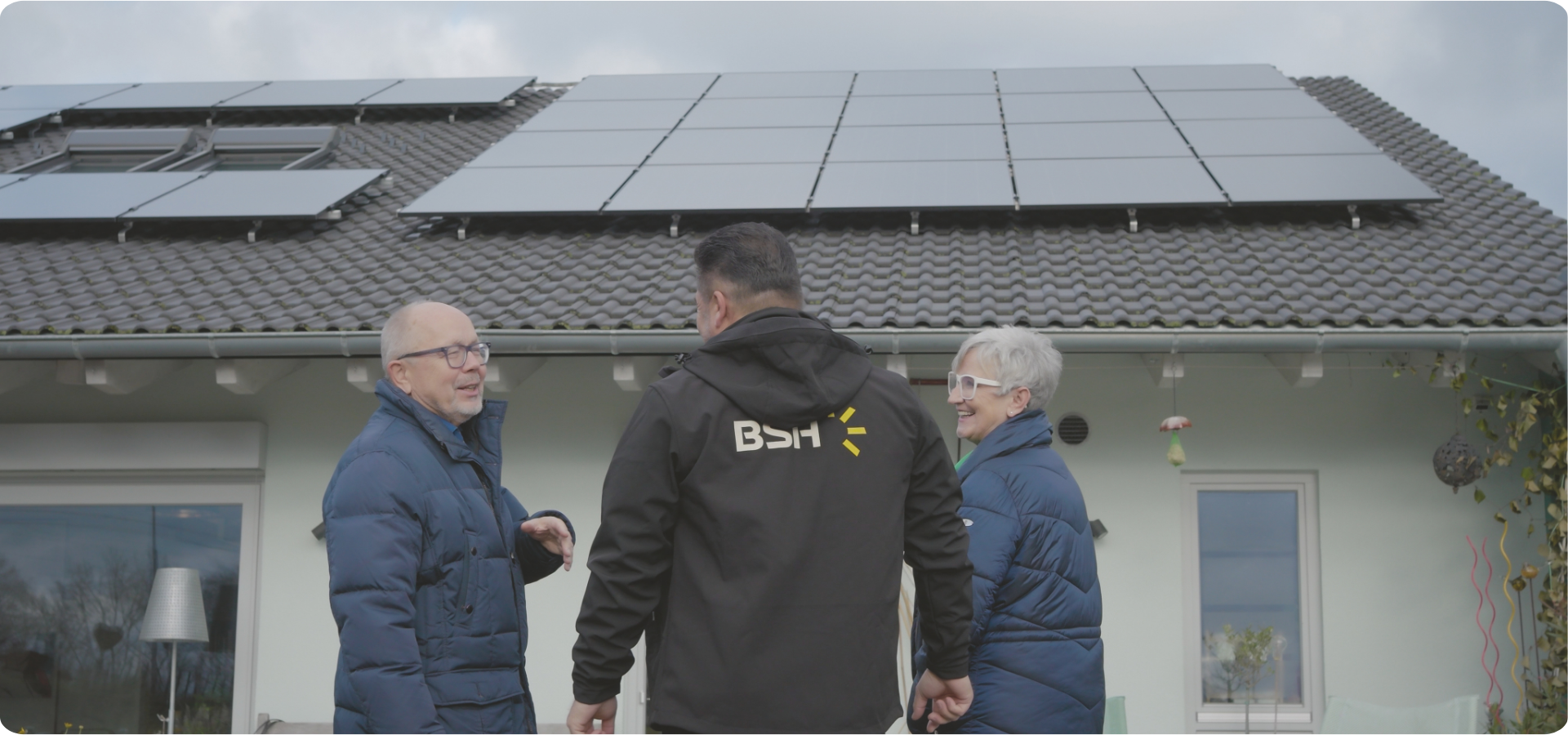 Glückliches älteres Ehepaar mit Fachberater vor ihrem Einfamilienhaus mit PV-Anlage