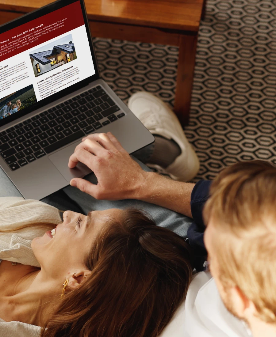 Junges Pärchen liegt auf der Couch und informiert sich am Laptop über die BSH Finanzierung.