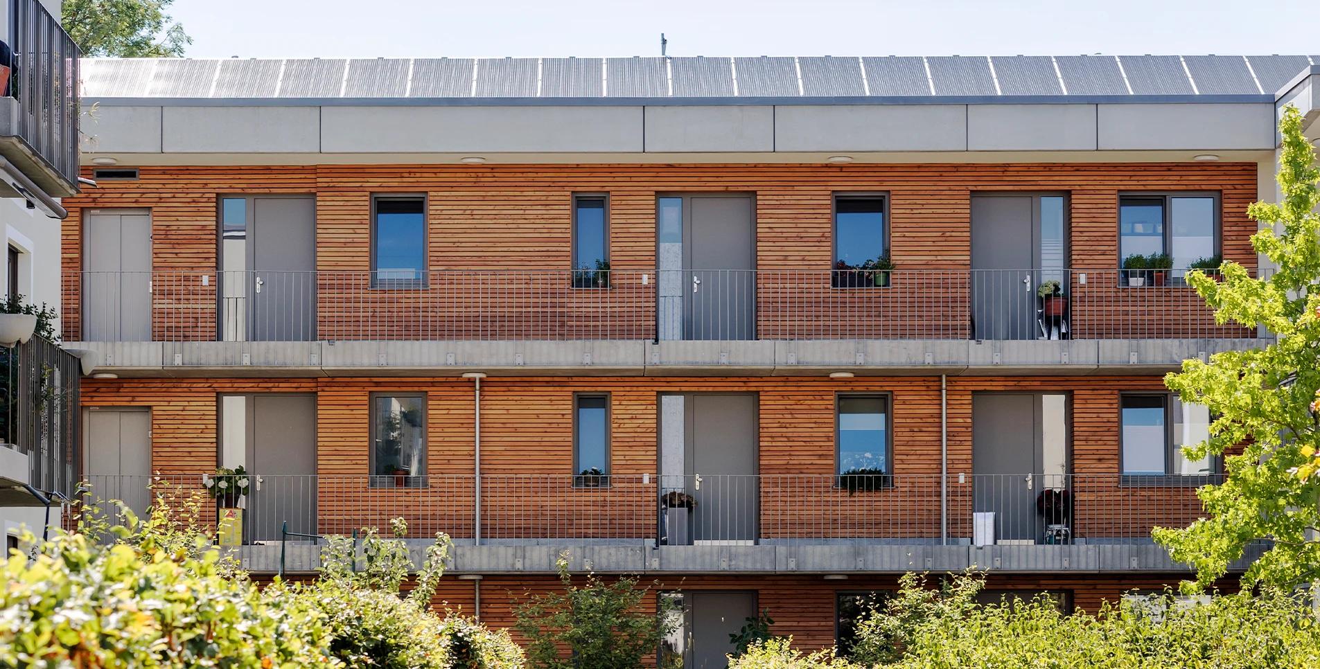 Fassade eines modernen Mehrfamilienhauses mit Holzverkleidung und Photovoltaikanlage auf dem Dach.